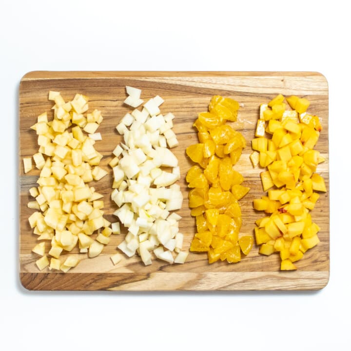 A wooden cutting board on a white background with chopped fruit ontop.