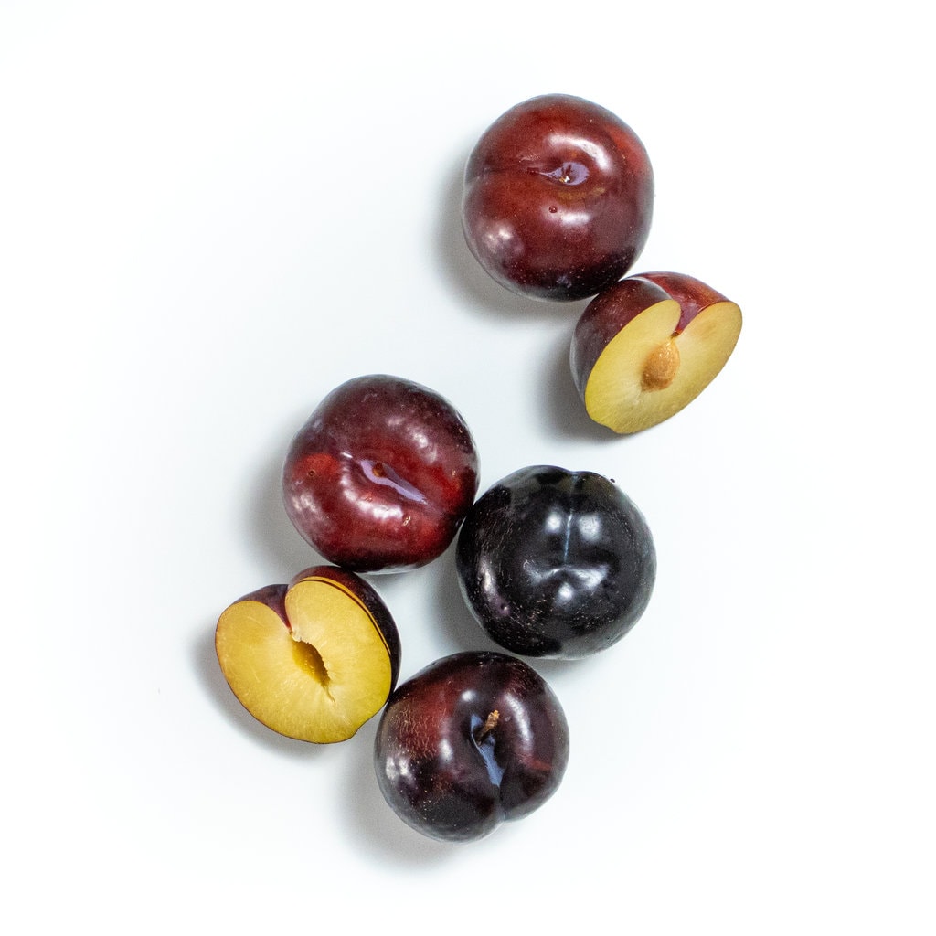 Plums scattered on a white countertop.