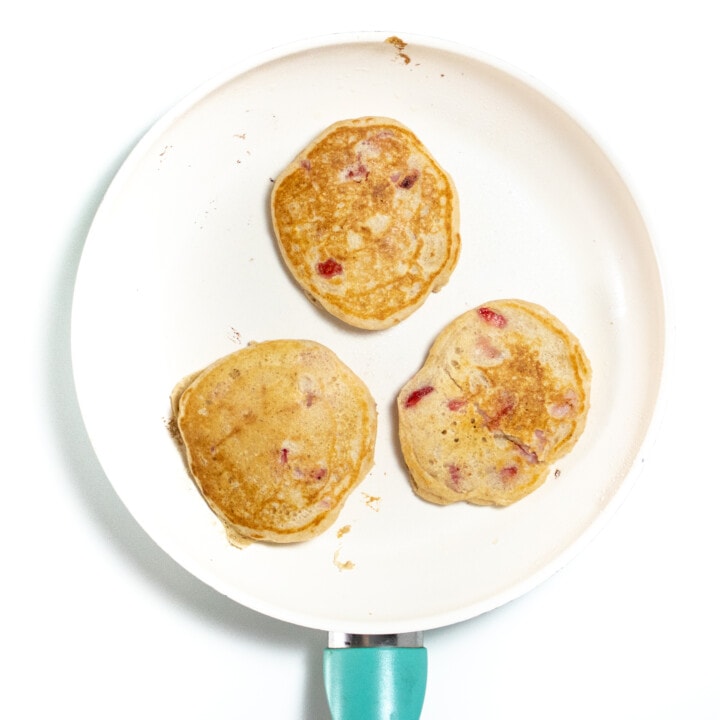 Medium skillet with 3 strawberry pancakes cooking.