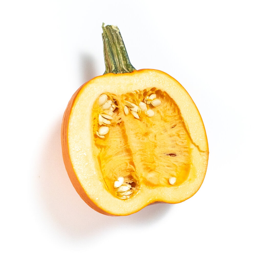 half of a pumpkin with the seeds sitting on a white counter.