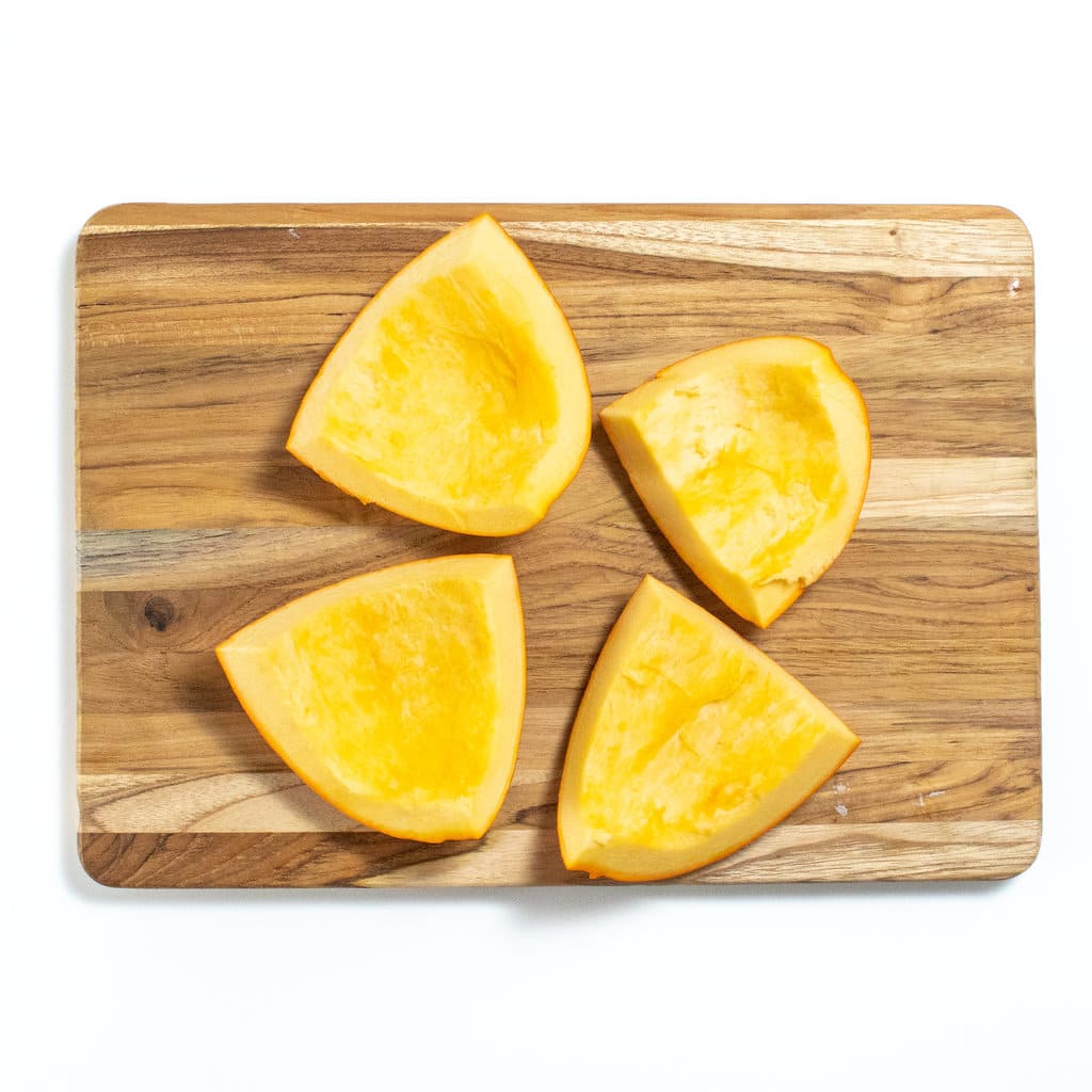 A wooden cutting board with chunks of pumpkin.