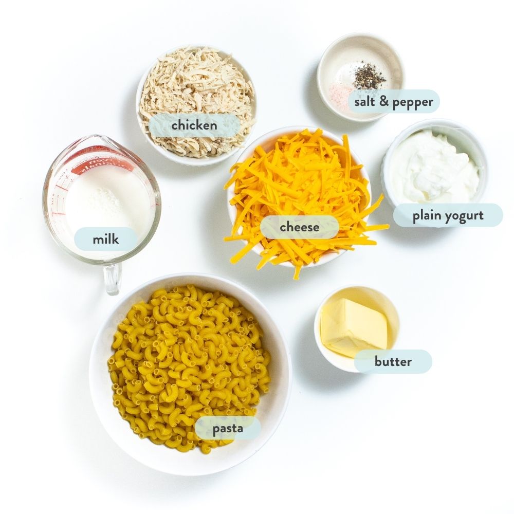 Ingredients for chicken, mac & cheese, and small white bowls with graphic labels, telling them what they are against a white countertop.