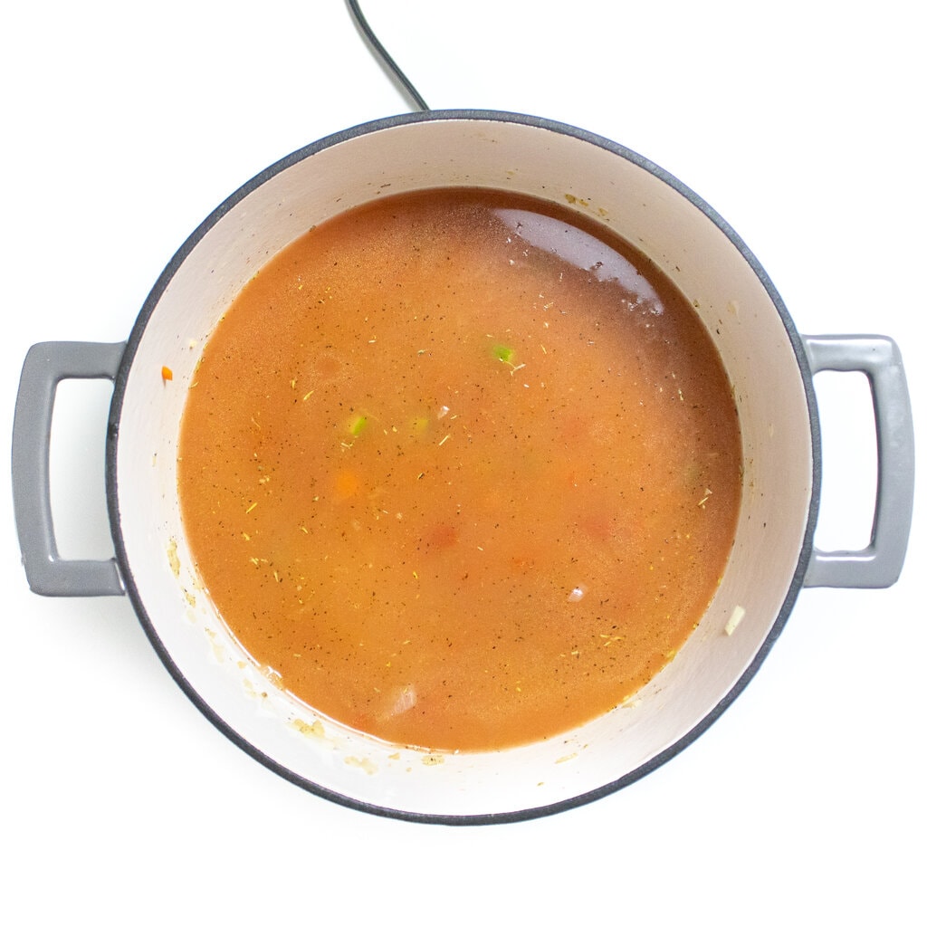 Gray stockpot with broth and ingredients for alphabet pasta.