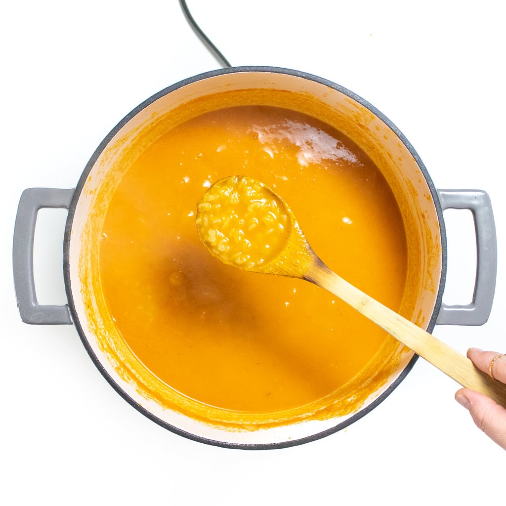 A large gray stockpot on a white countertop with a wooden spoon, showing the cooked alphabet pasta.