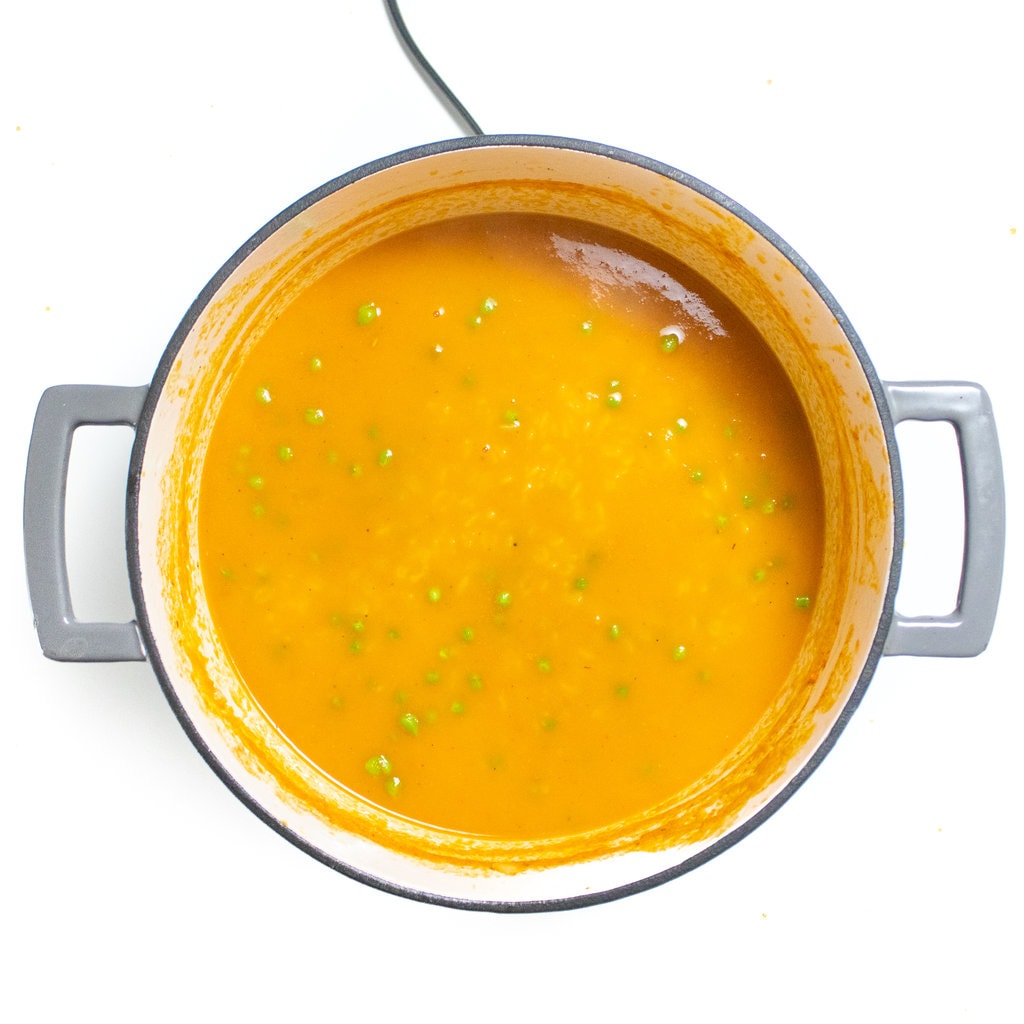 A large gray stockpot with the ingredients of simmering alphabet pasta soup.