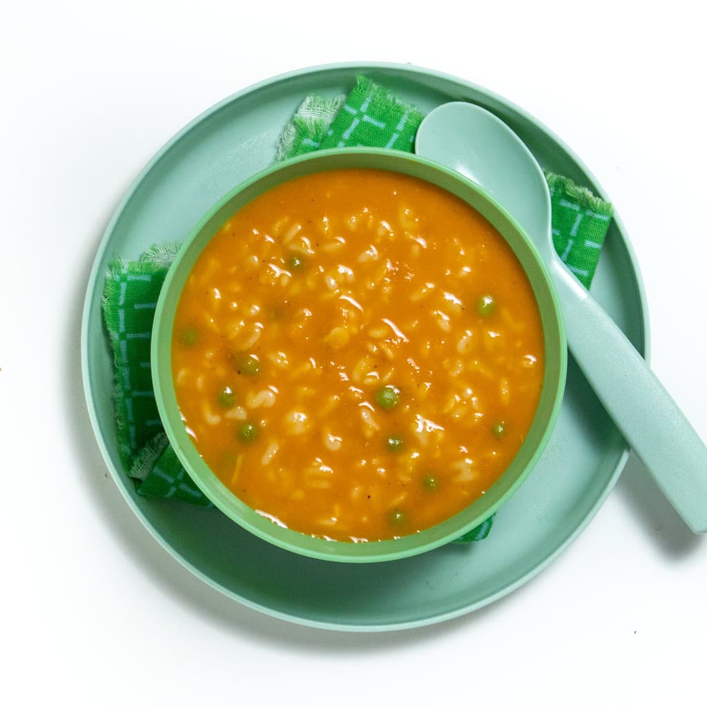 Green and teal plate and bowl for kids all of alphabet soup with a teaspoon resting on the plate.