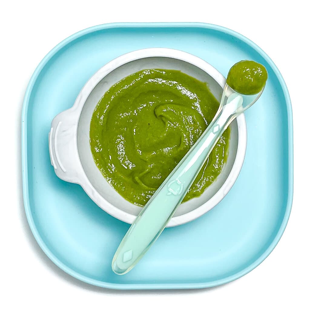 Teal baby plate with gray baby bowl with asparagus. Purée on top with a teal spoon resting on top.