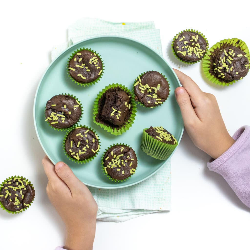 Two kids hands holding a kids to your plate full of avocado, brownie bites.