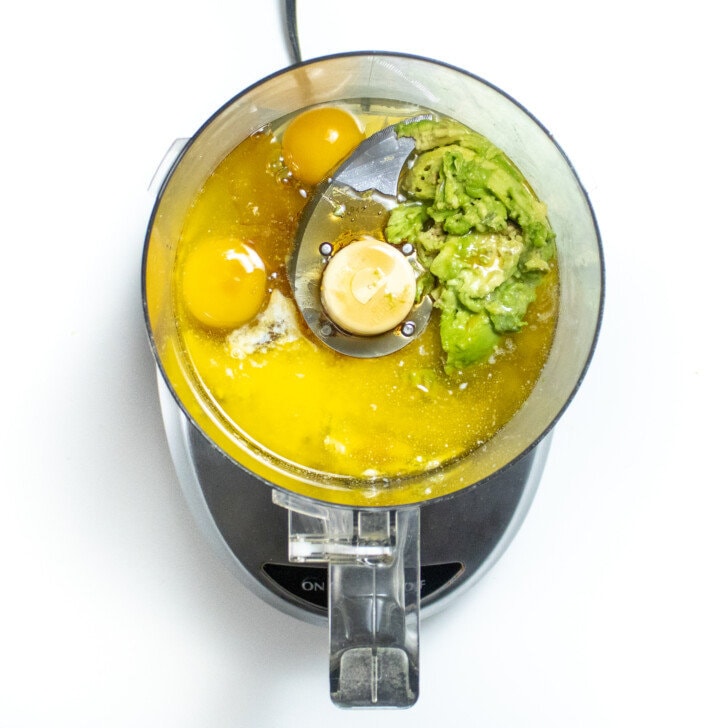 A food processor on the way background full of wet ingredients for avocado brownies.