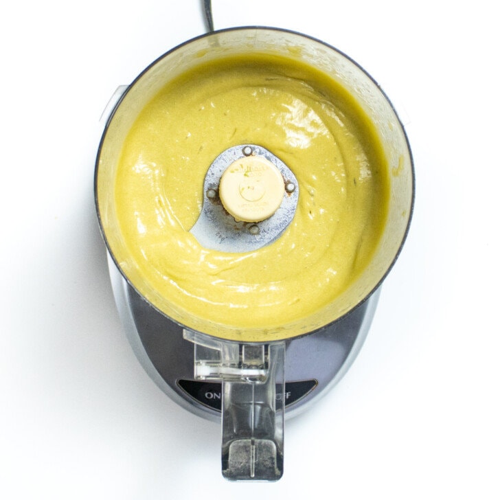 A food processor on the way background with creamed ingredients for avocado brownies.