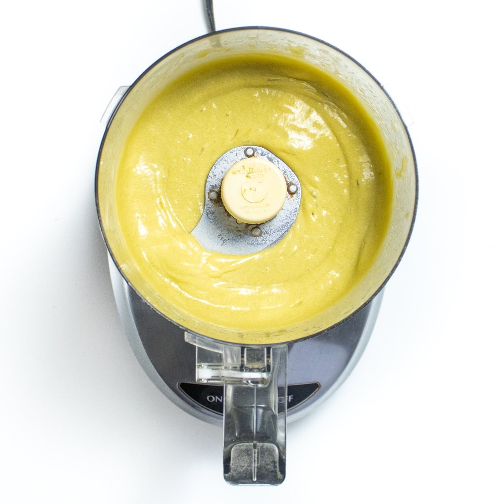 A food processor on the way background with creamed ingredients for avocado brownies.