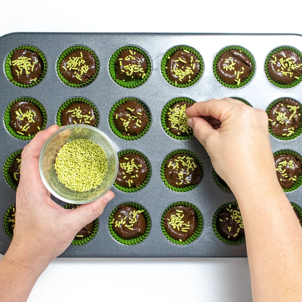 A hand sprinkling on sprinkles on brownie bites.