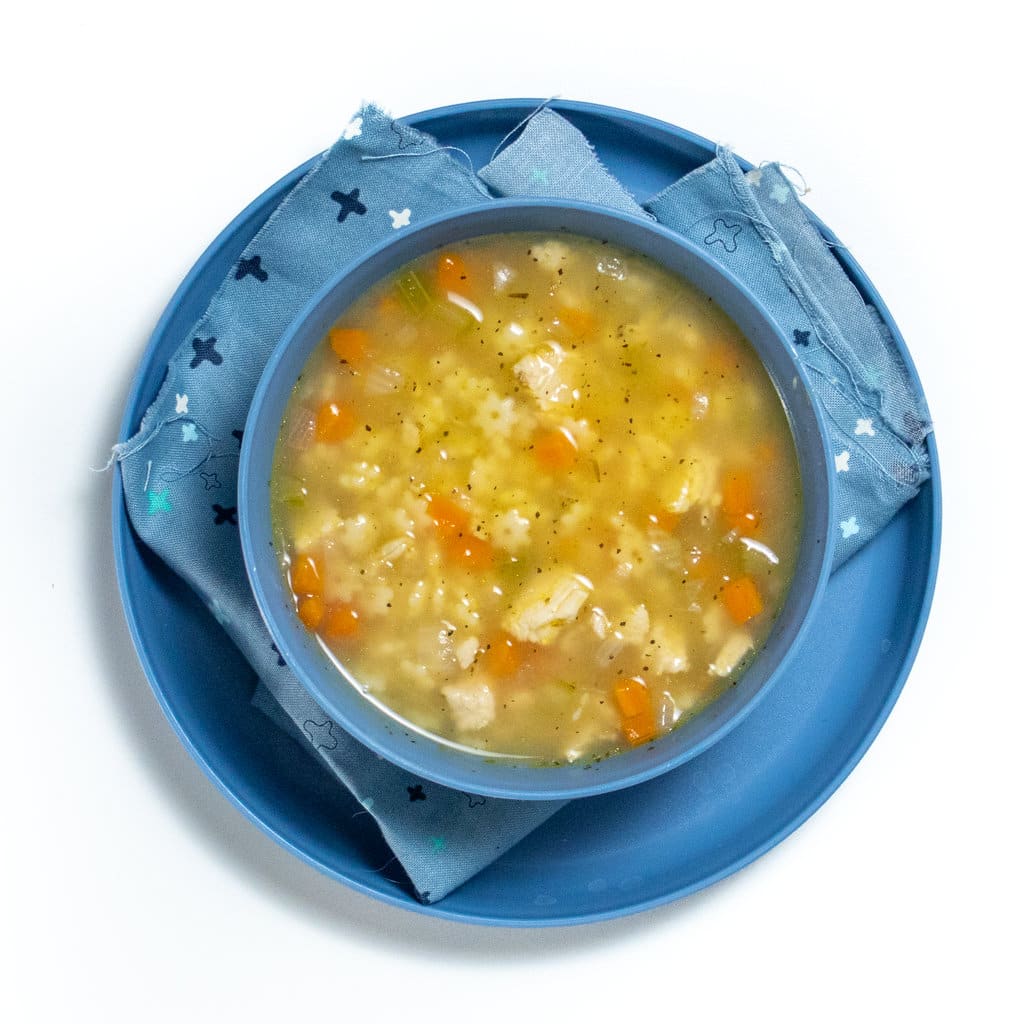 Blue kids all and played with a colorful blue napkin with chicken and star soup inside of the bowl.
