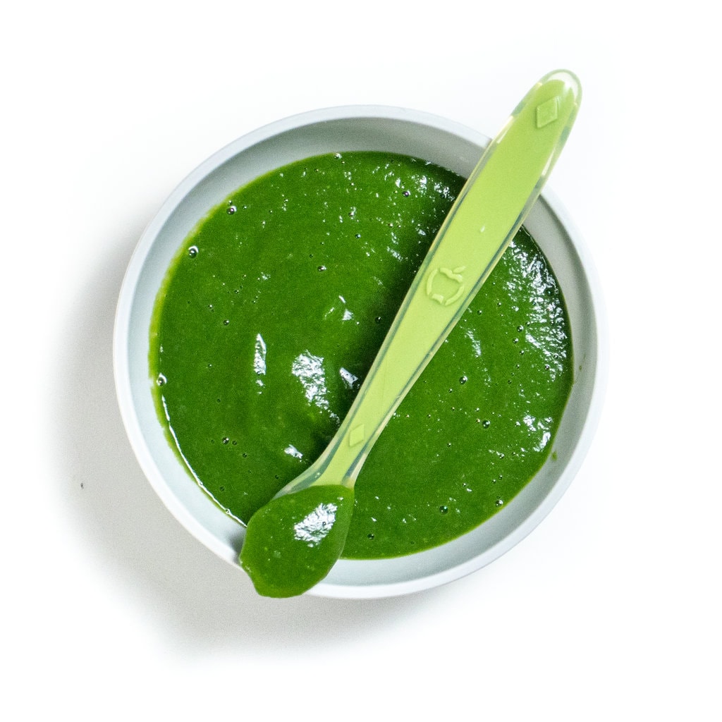 Gray baby bowl with puréed, spinach and green beans with a green spoon on top with a purée in it.