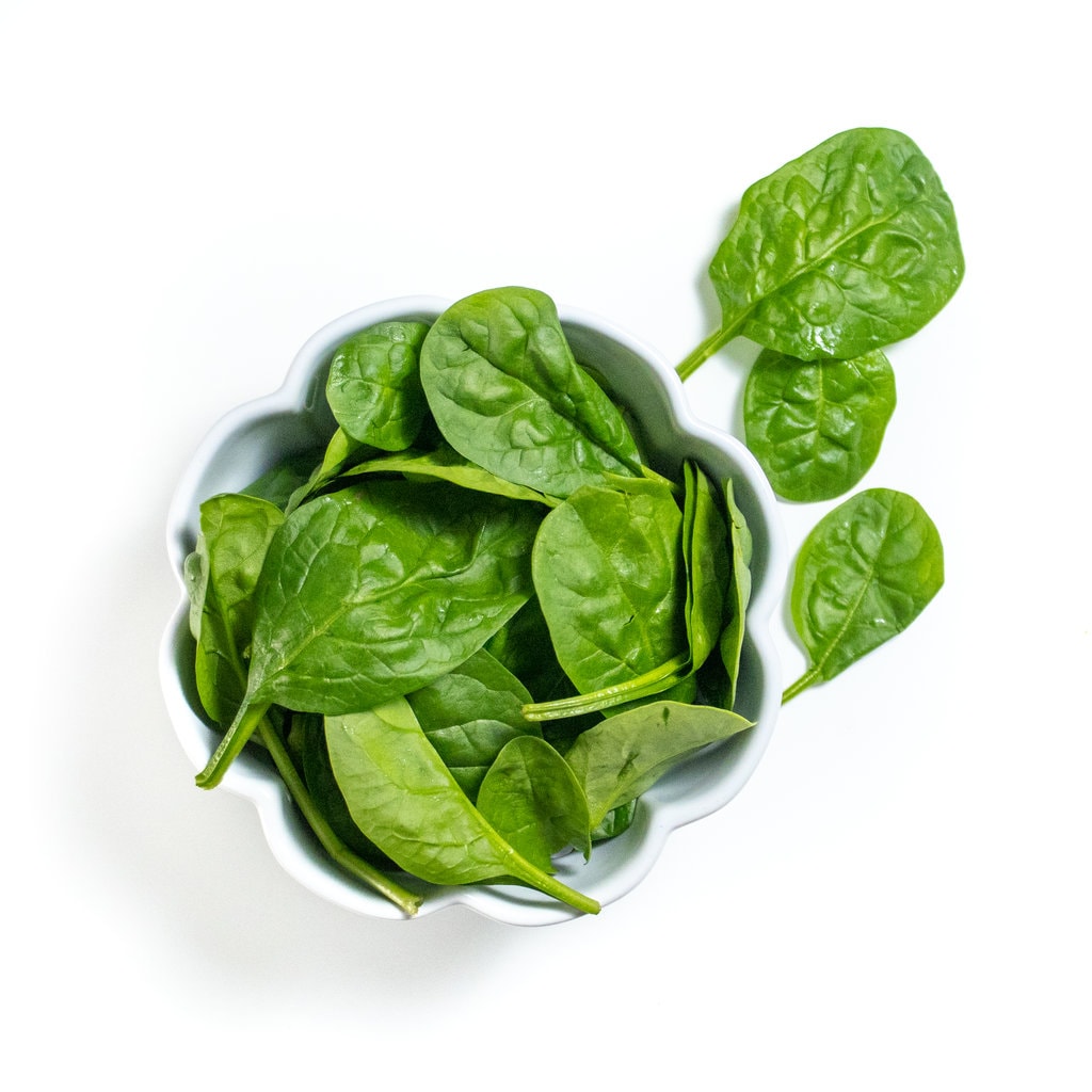 White bowl full of baby spinach on a white countertop.