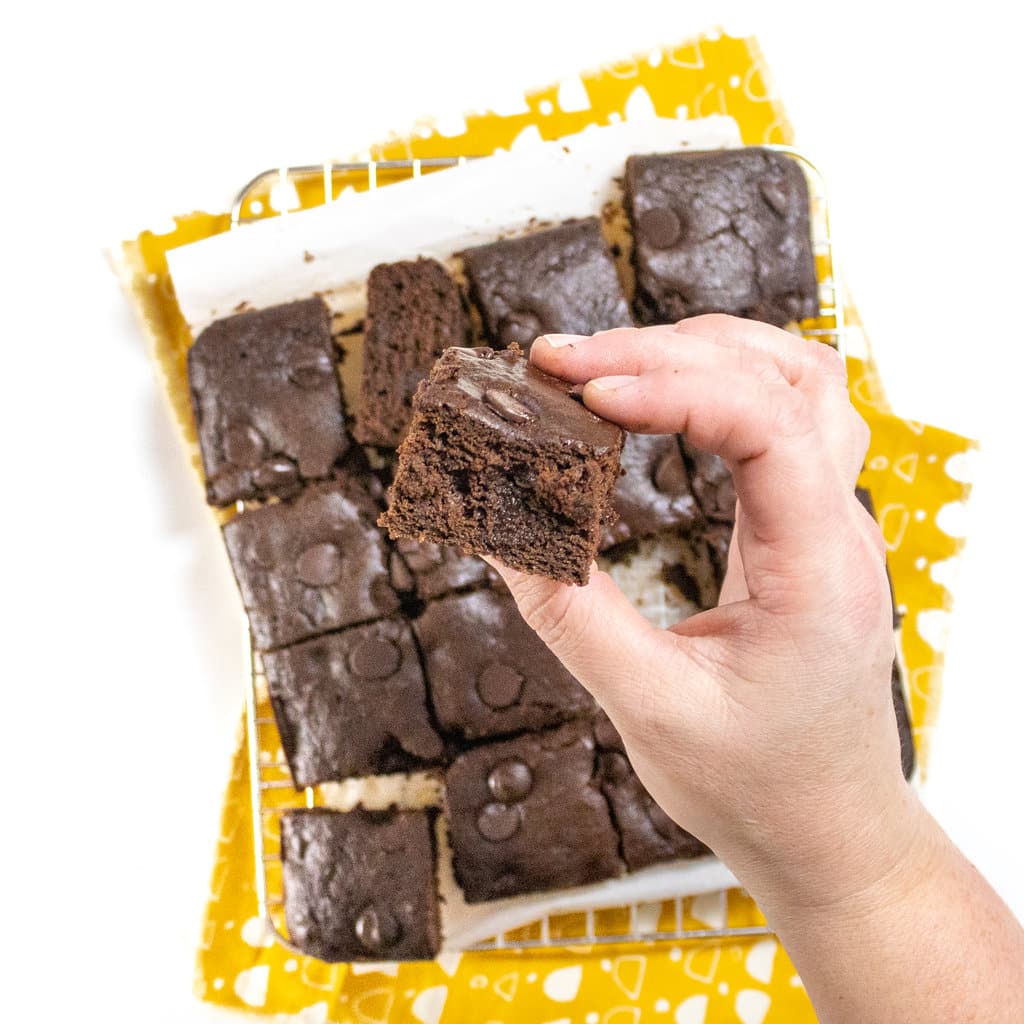A small cooling rack with squares of cut, sweet potato brownies with a hand, holding one up to show how fuckhead is.