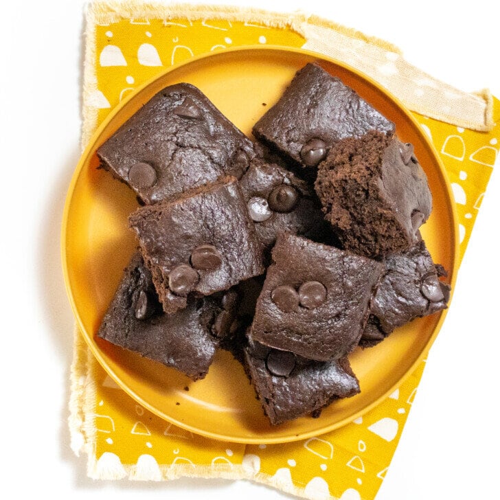 mustard yellow kids play with a yellow white countertop. The plate is full of square cut sweet potato brownies for kids.