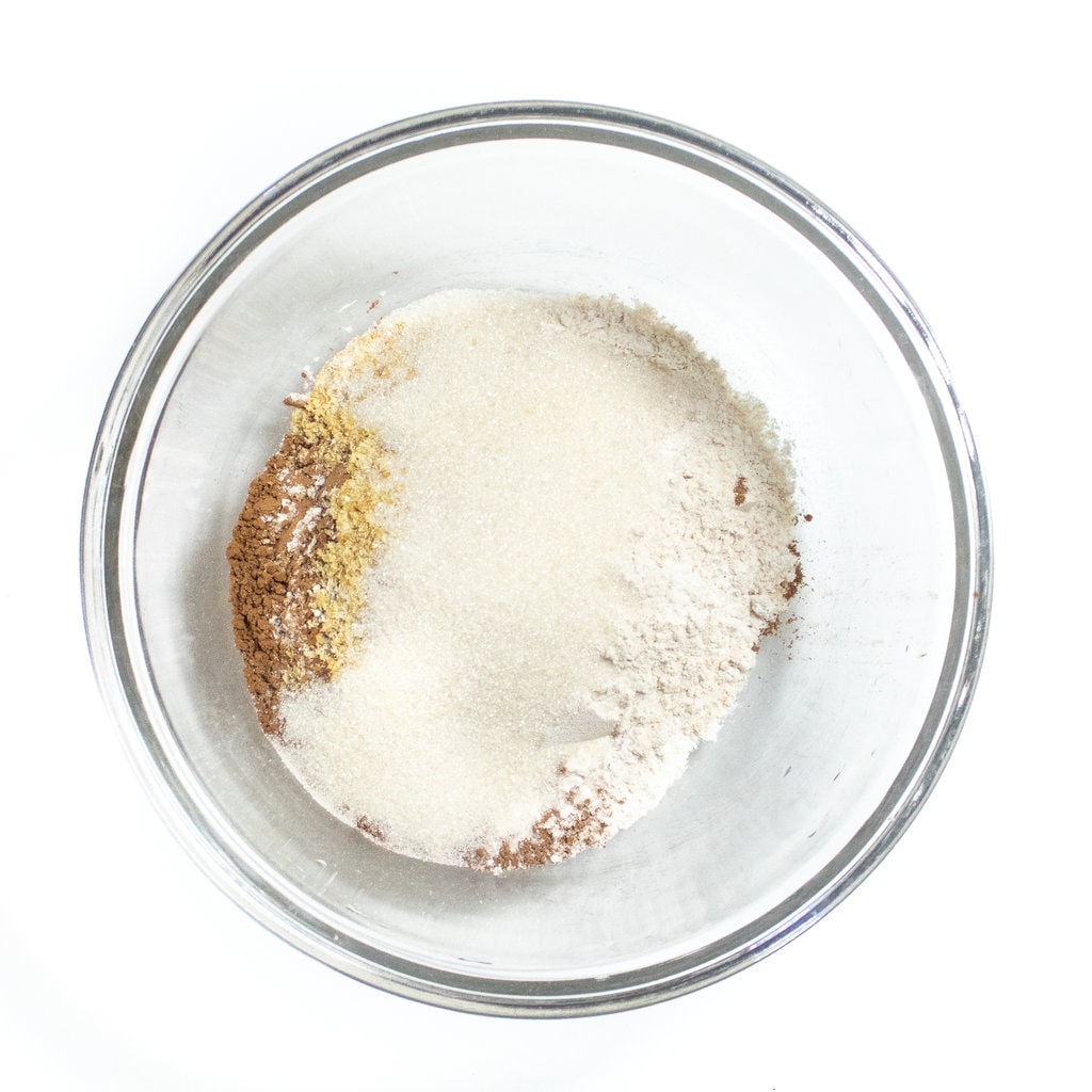 Glass mixing bowl on a white counter full of dry ingredients for sweet potato brownies.