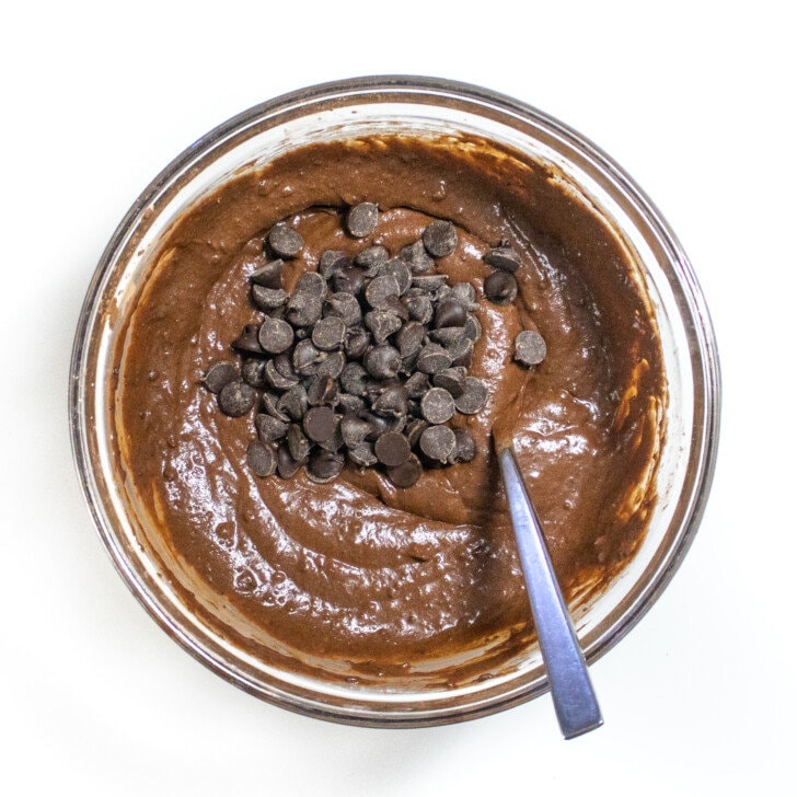 Clear mixing bowl on white countertop with sweet potato brownie batter with chocolate chips on top.