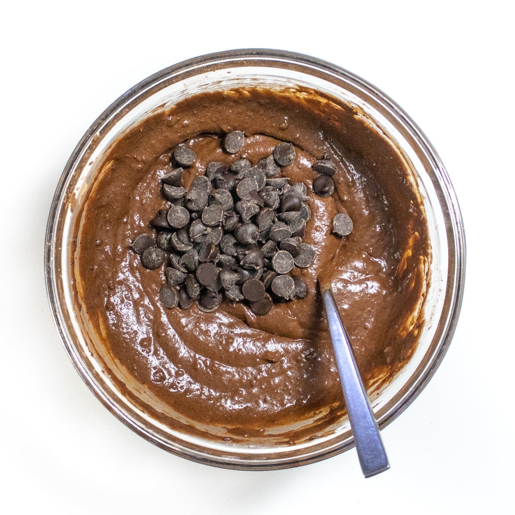 Clear mixing bowl on white countertop with sweet potato brownie batter with chocolate chips on top.