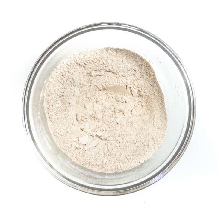 Clear mixing bowl on a white countertop with dry ingredients for whole wheat pancakes.