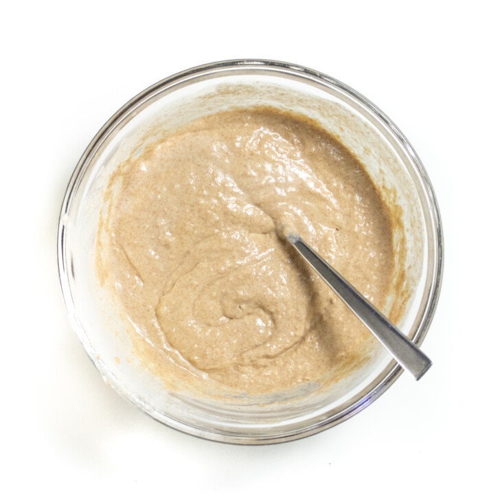 Clear mixing bowl on a white countertop with wet and dry ingredients for whole wheat pancakes.