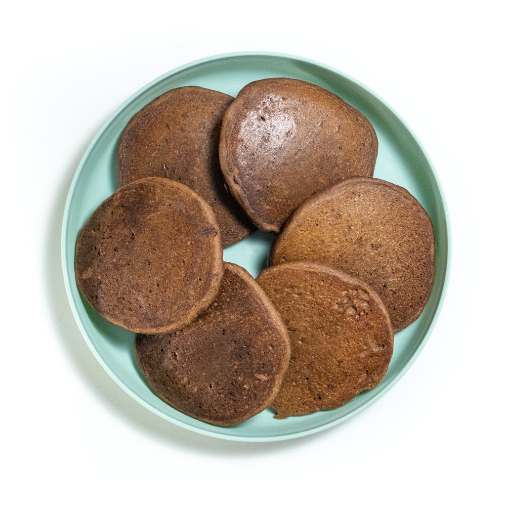 Teal kids plate on the white countertop with a bunch of chocolate pancakes on top.