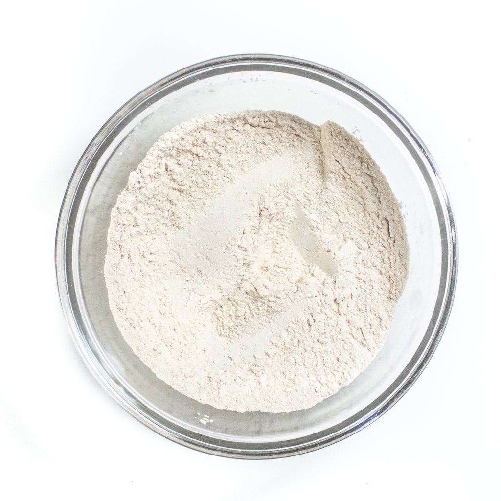 Clear mixing bowl on a white counter with dry ingredients for muffins.