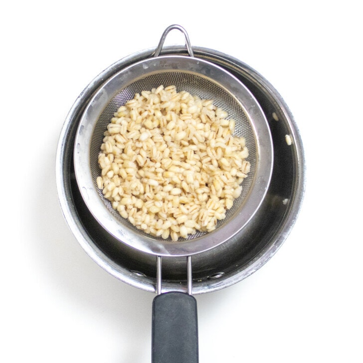 Cooked barley been strained over a sauce pan.
