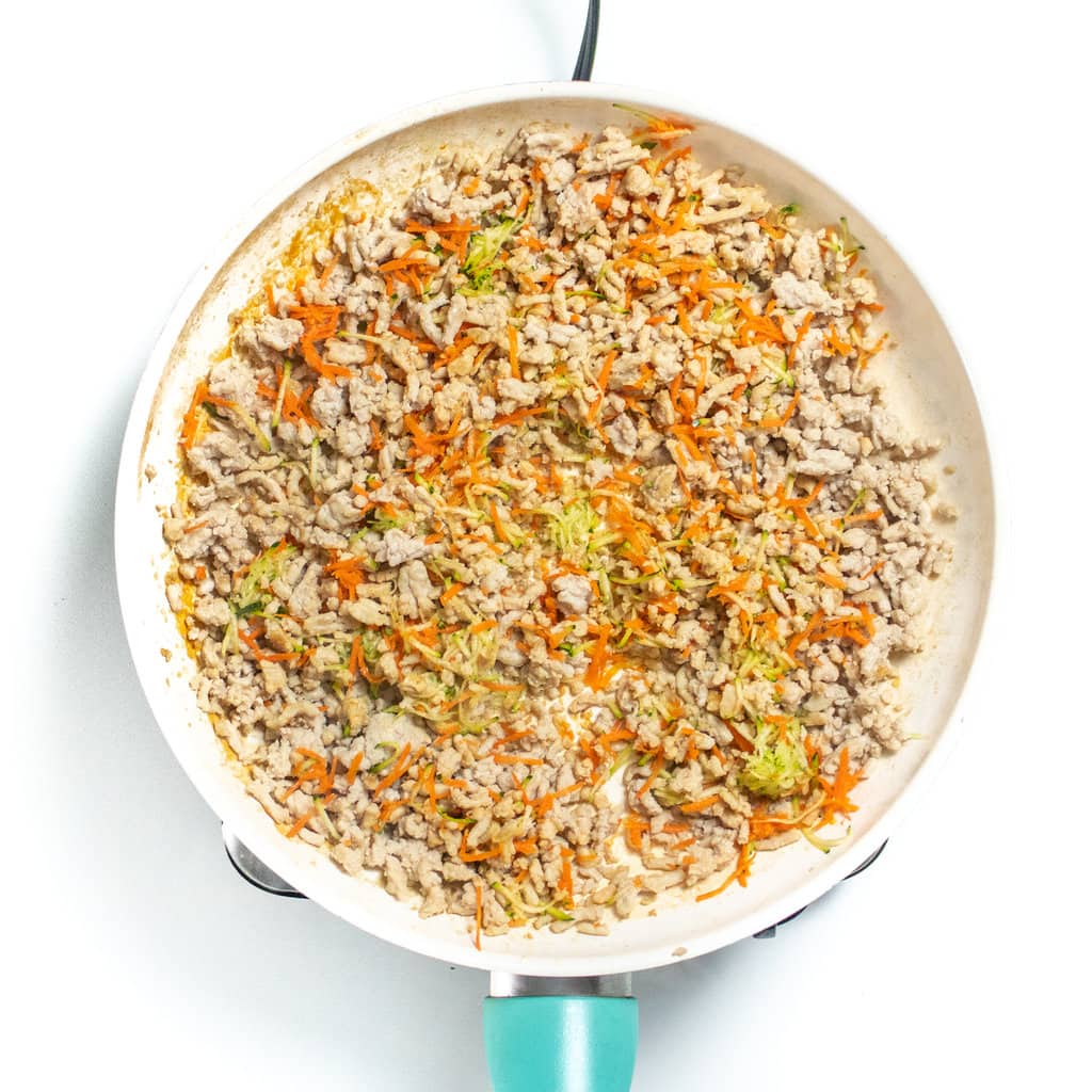 A medium white skillet with ground chicken, grated zucchini, and grated carrots cooking for soft tacos.