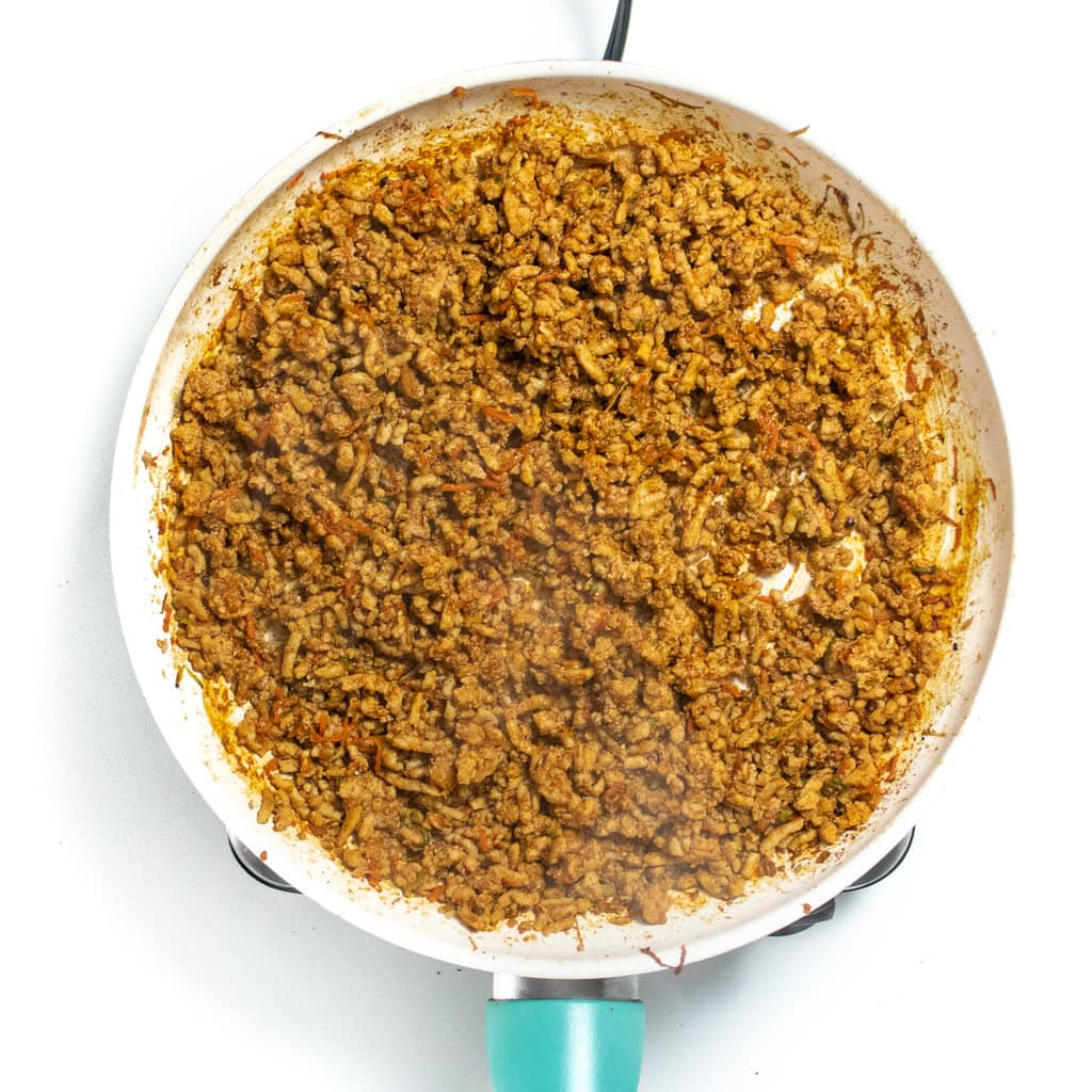 A white skillet full of cooked ground chicken with spices for soft tacos.