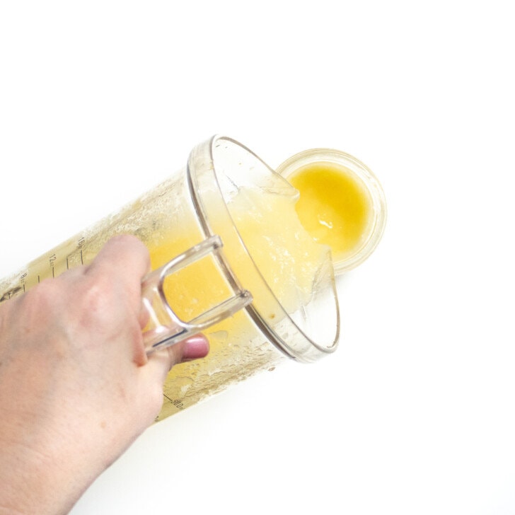 Hand pouring an apple and orange puree into a small glass jar.