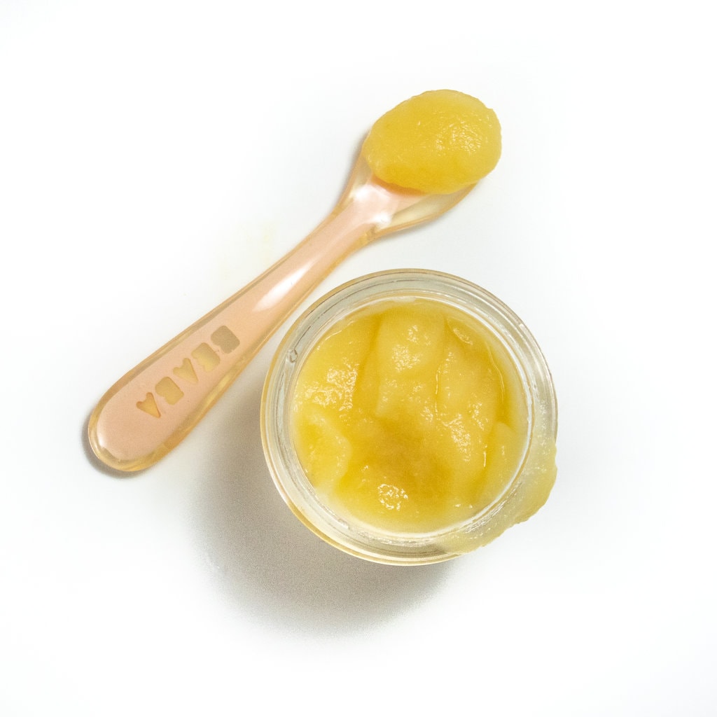 Small glass jar on a white countertop with apple and orange puree.