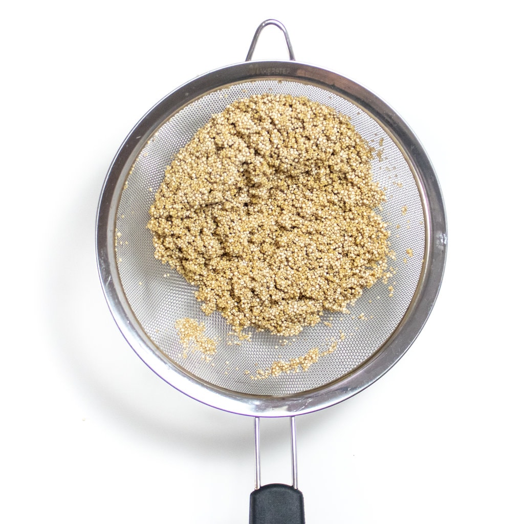 A silver fine mesh colander with rinsed quinoa over a white counter.
