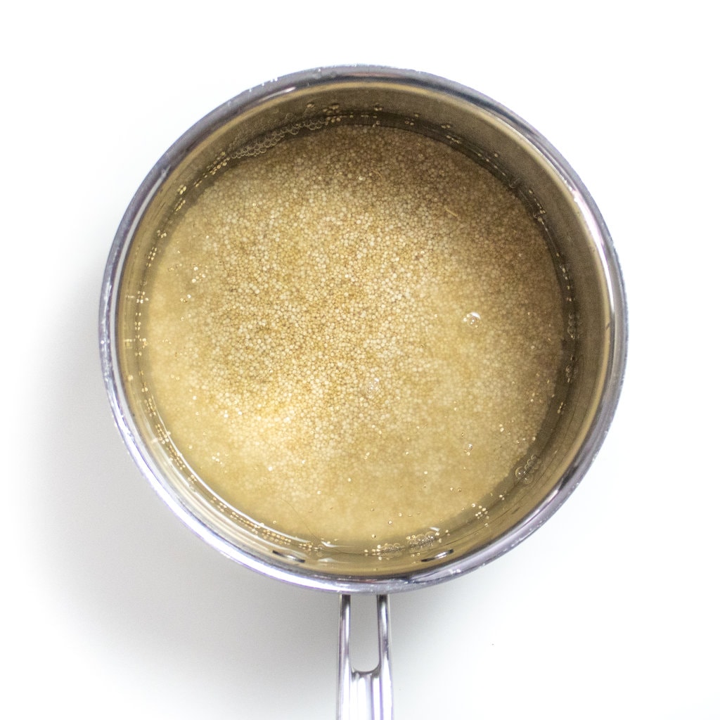 A silver sauce, pan with water and dry quinoa, ready to be cooked sitting on a white counter.