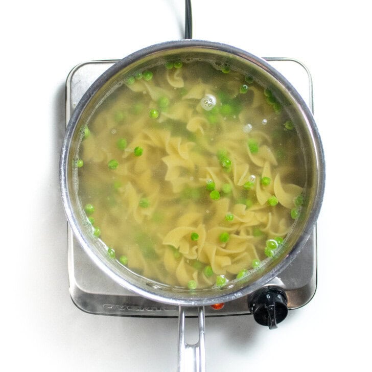 Silver sauce, pan with egg noodles and peas, cooking and boiling water.