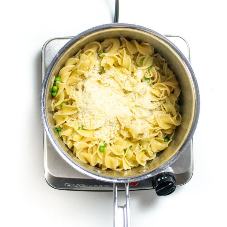 Silver sauce, pan with cooked egg, noodles, peas, and a sprinkling of Parmesan with butter.