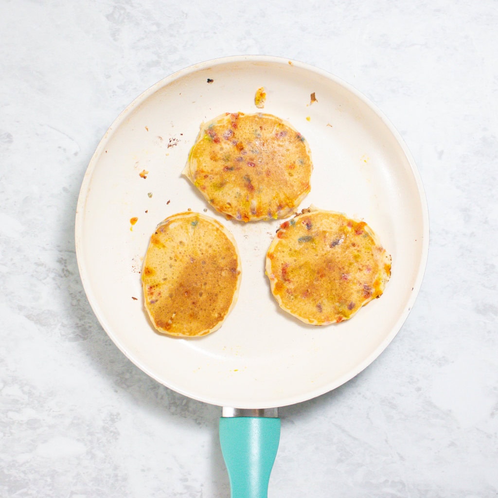 Small white skillet with blue handle sitting on my white kitchen counter with 3 small funfetti pancakes.