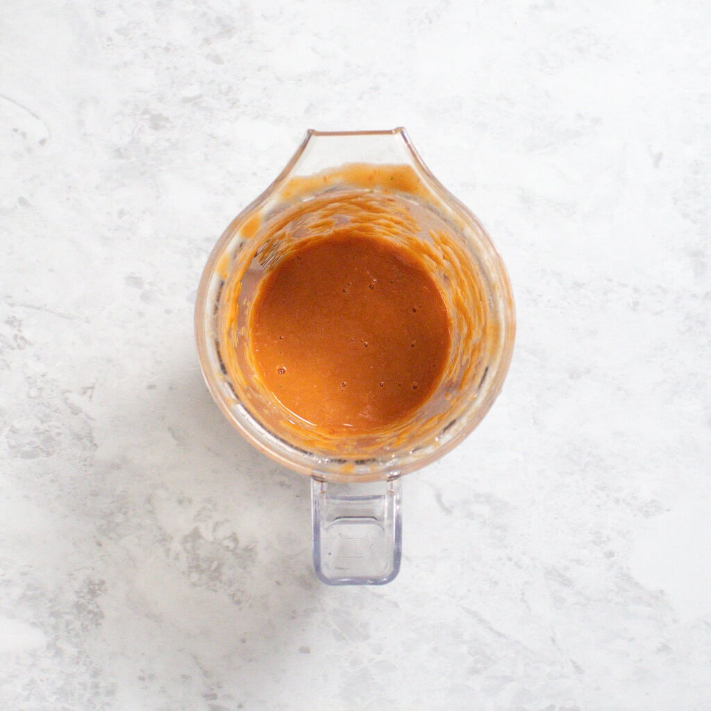 Small clear blender on white countertop with pureed tomato and basil inside.