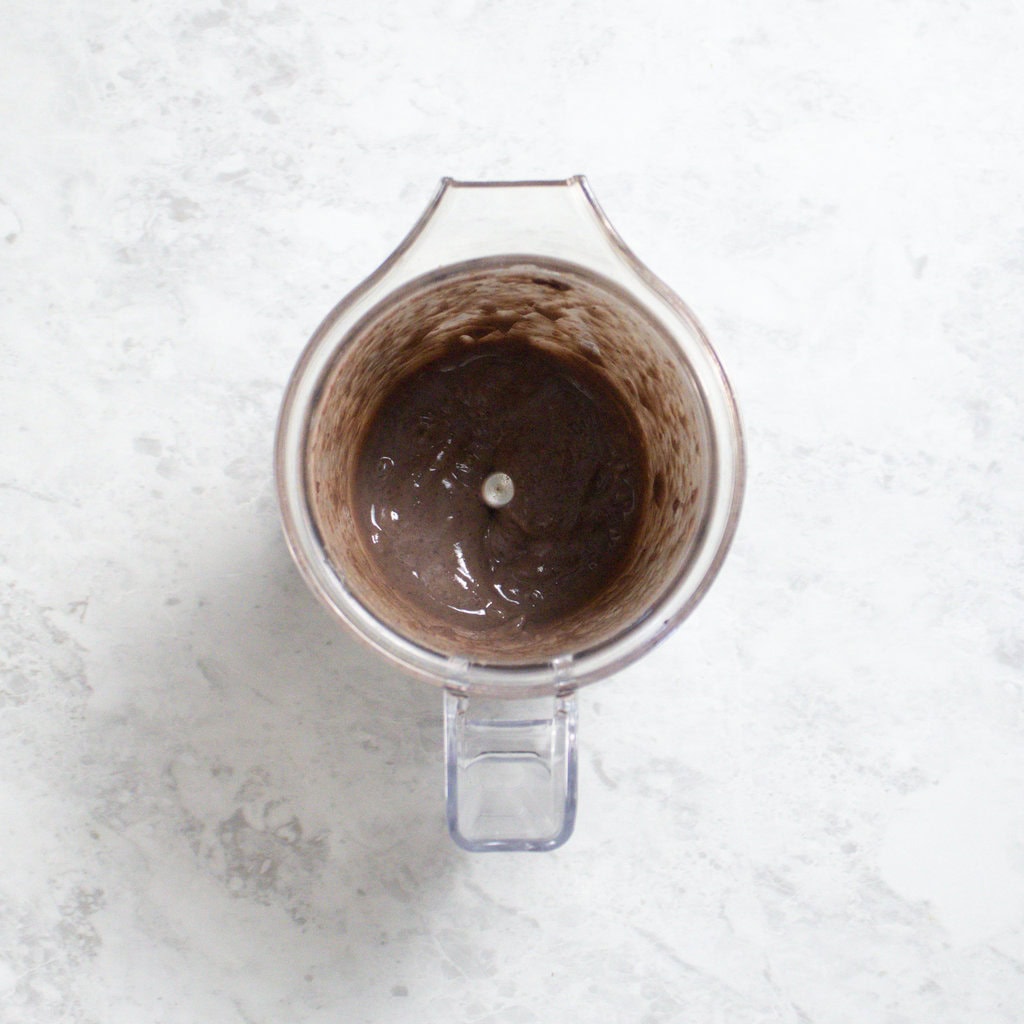 Small clear blender sitting on my white kitchen counter with black bean puree for baby.