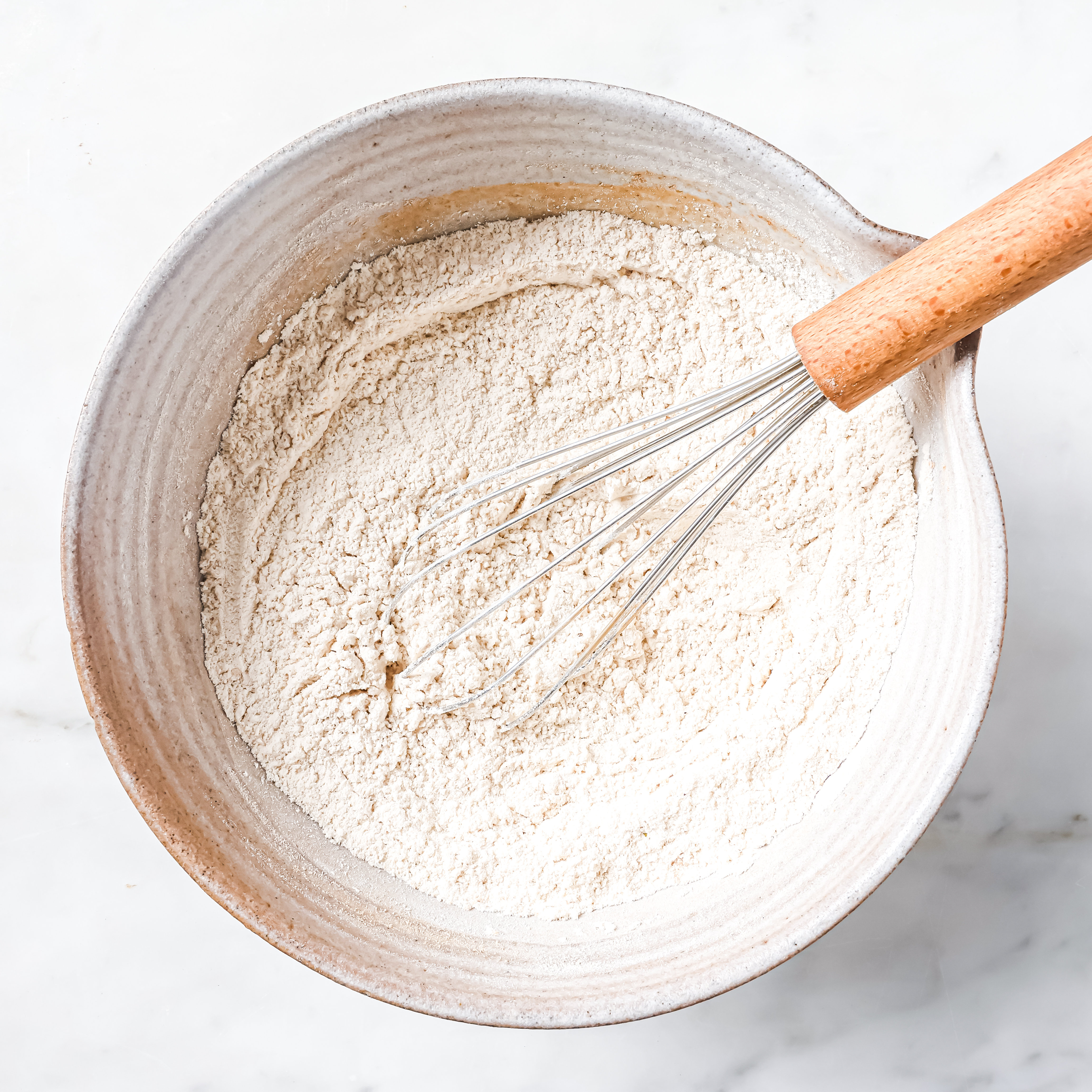 White mixing bowl on kitchen counter with whisked dry ingredients.