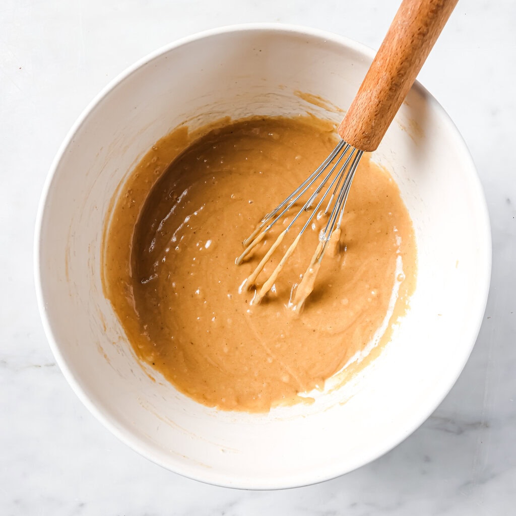 White mixing bowl on my kitchen counter with whisked batter for carrot cake muffins.
