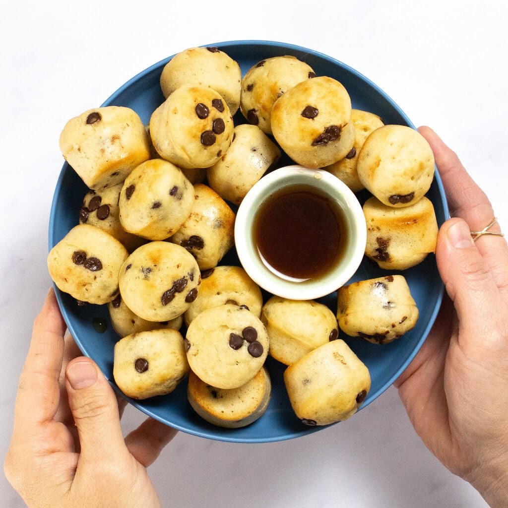 My hands holding a blue kids plate that is full of golden brown mini pancake bites.
