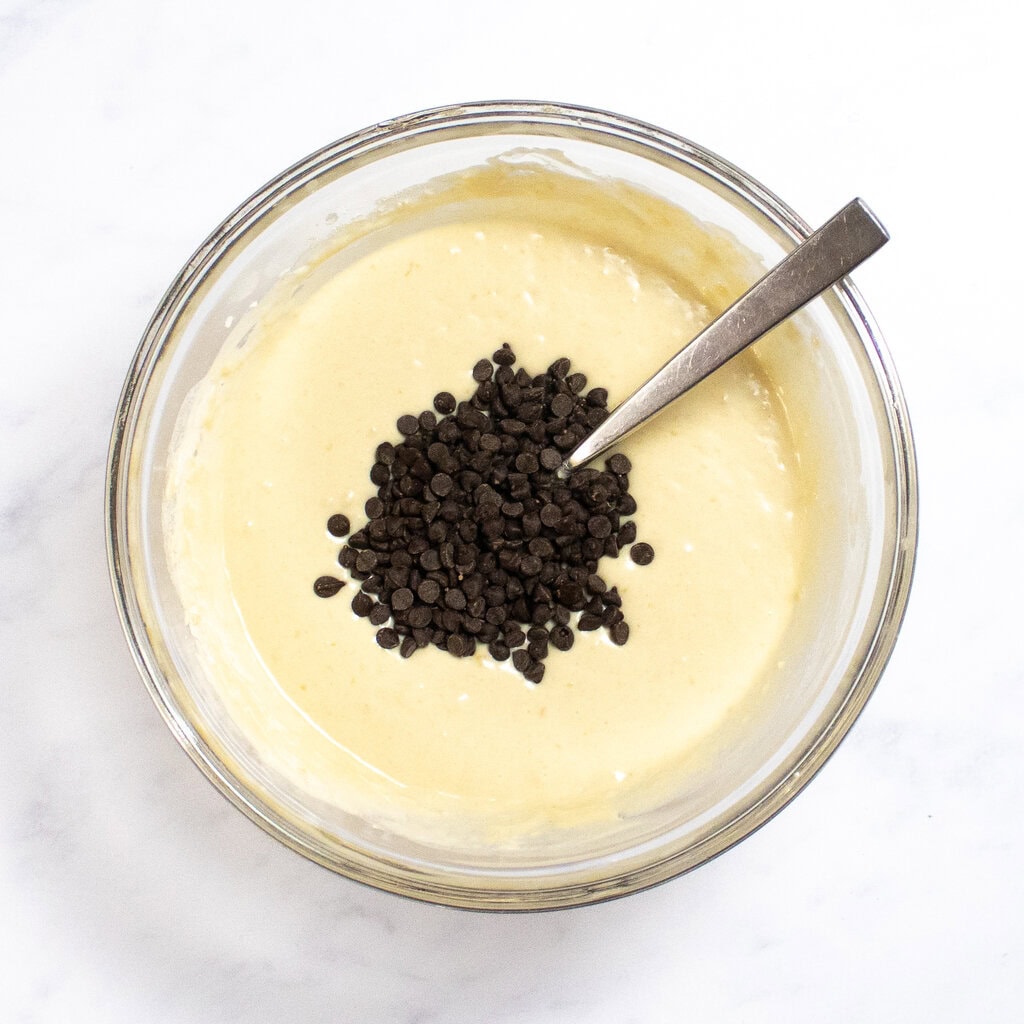 A clear glass mixing bowl with pancake batter with chocolate chips ready to get mixed in.